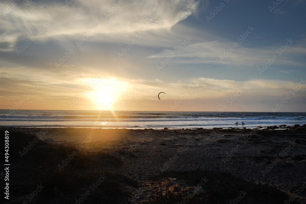 A kiteboarder and two surfers enjoying their time at Jalama Beach, during sunset over the Pacific Ocean, in Santa Barbara County, California.