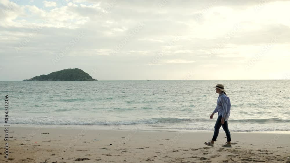 Side view young woman with hat walk into the sea with sunset moment. Happy female relaxing on vacation time holiday weekend after hard work all day. Travel and resting on the beach concept. Side view young woman with hat walk into the sea with sunset moment. Happy female relaxing on vacation time holiday weekend after hard work all day. Travel and resting on the beach concept.
