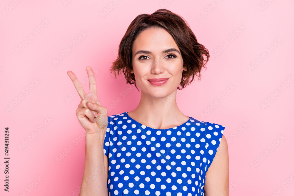 Photo of young pretty girlish female in blue dotted apparel showing v-sign isolated on pink color background Photo of young pretty girlish female in blue dotted apparel showing v-sign isolated on pink color background