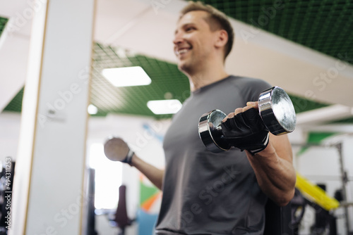 Attractive Caucasian blonde man lift heavy dumbbells in the gym. Personal workout hour. Daily sport and health exercises