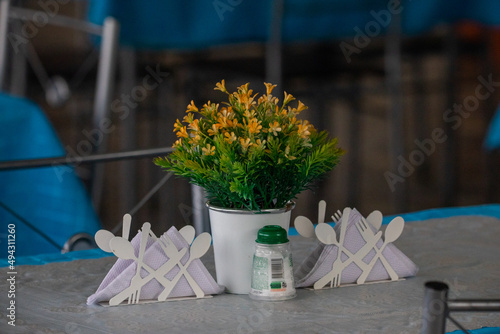 Beautiful photo of a decoration composition in a cafe, orange flowers in a pot, standing on the table, on both sides of a spoon and fork, salt