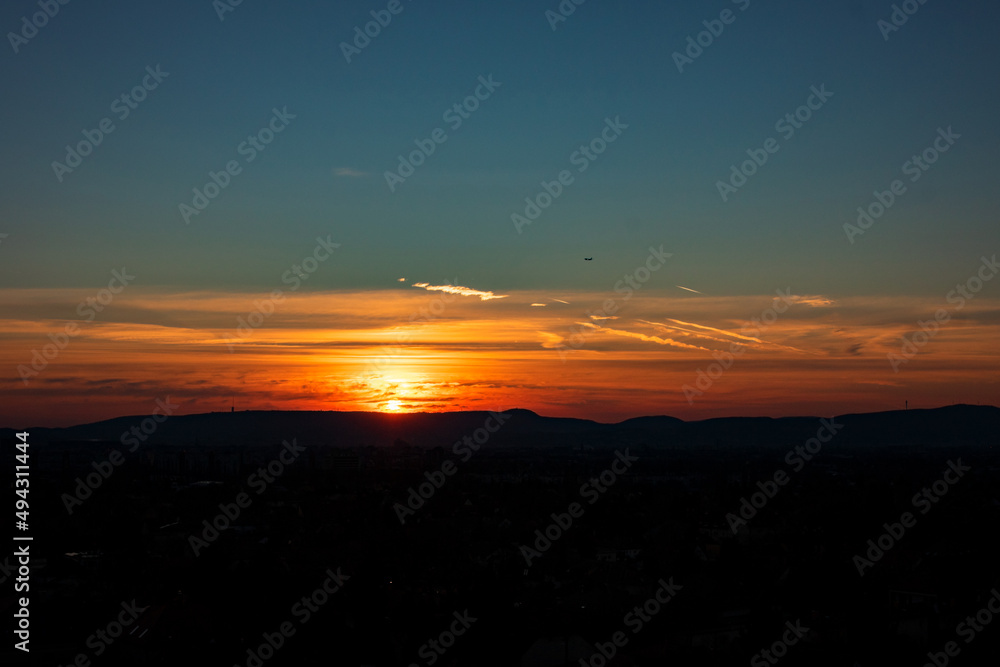 Sunset sunrise at city with bright colorful dramatic sky and dark ground with silhouettes of mountains