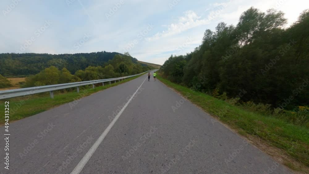 Aerial FPV view of empty country asphalt road. Two multi-ethnic active young runners jogging together. Sport activity. Athletes. Countryside. Aerial FPV view of empty country asphalt road. Two multi-ethnic active young runners jogging together. Sport activity. Athletes. Countryside.