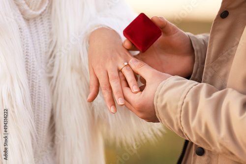 Young man putting ring on finger of his fiancee after marriage proposal outdoors, closeup