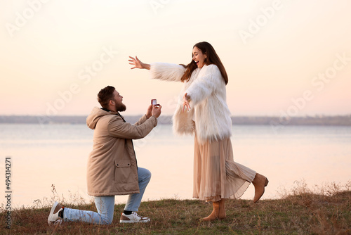 Young man proposing to his happy girlfriend near river