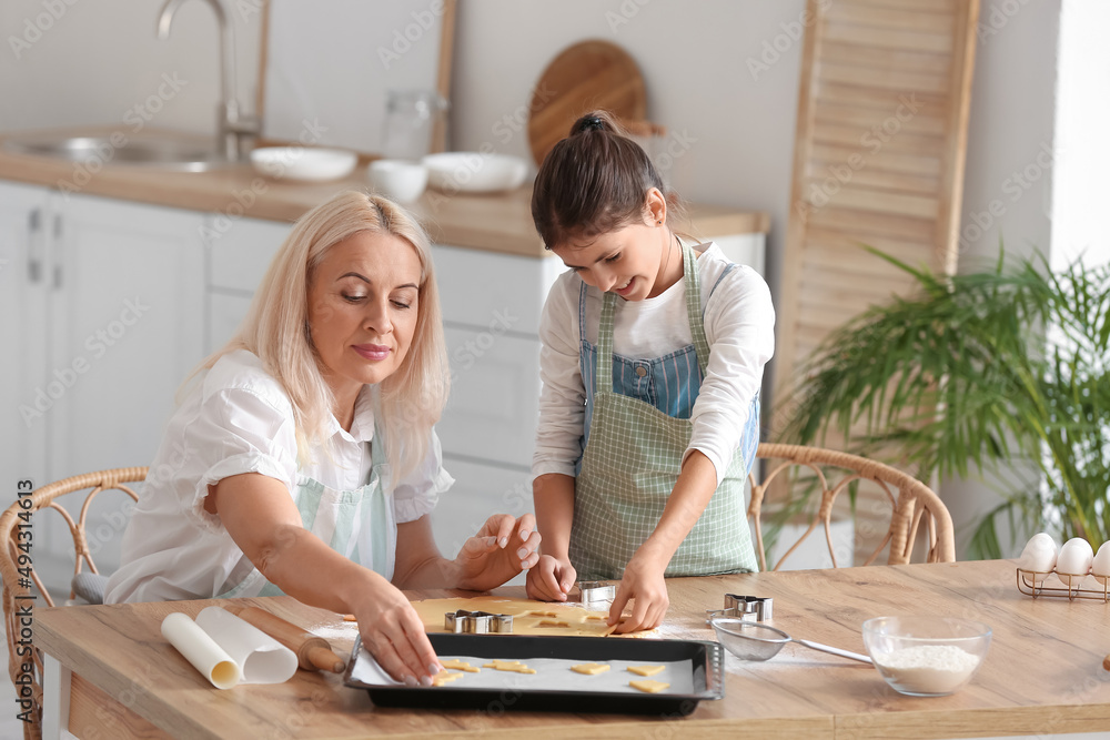 Fototapeta premium Mature woman and her little granddaughter cutting dough for cookies at table in kitchen
