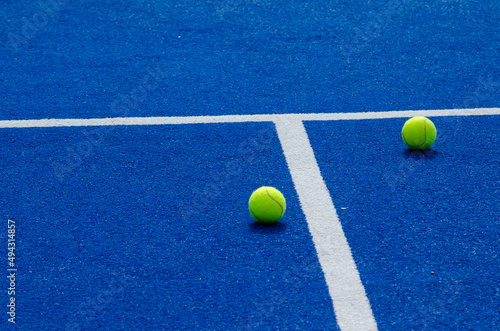 two paddle tennis balls near the lines of a blue paddle tennis court