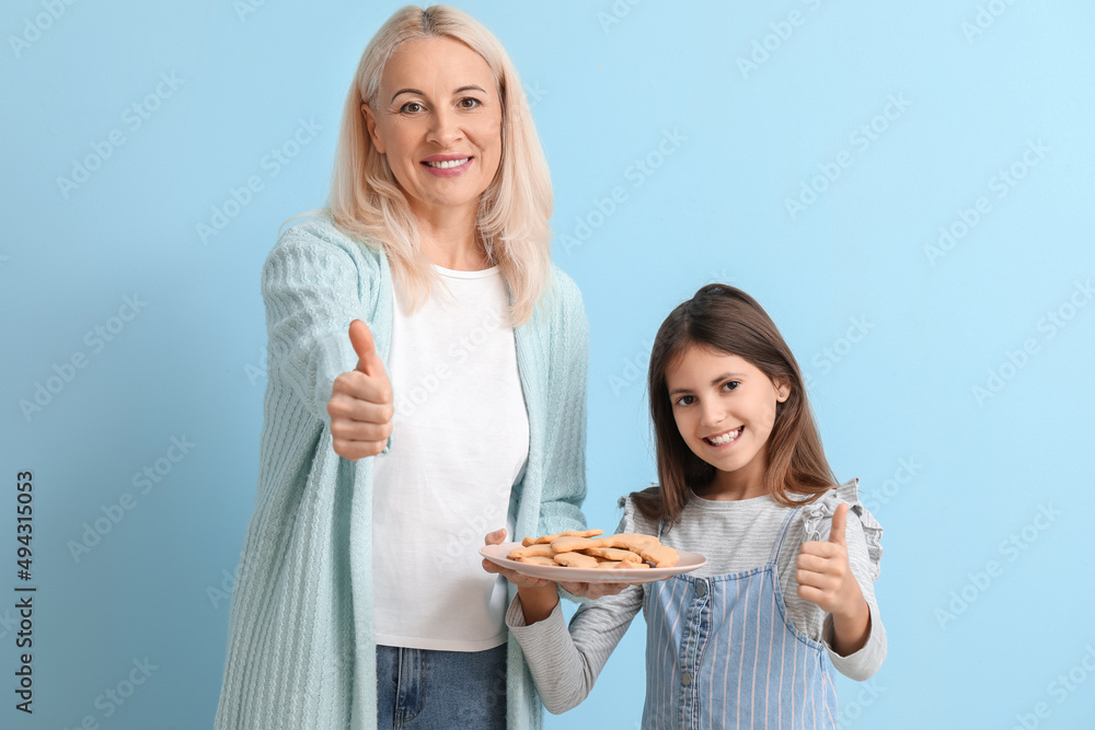 Mature woman and her little granddaughter with cookies on blue background Mature woman and her little granddaughter with cookies on blue background
