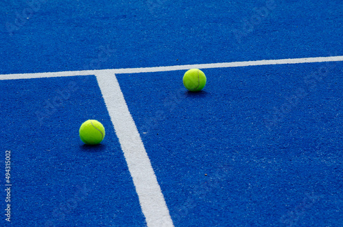two paddle tennis balls near the lines of a blue paddle tennis court