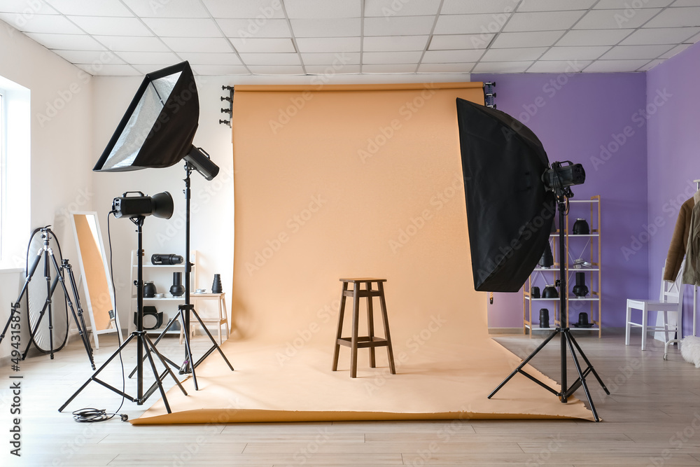 Lighting equipment, stool and beige cyclorama in modern photo studio - obrazy, fototapety, plakaty 