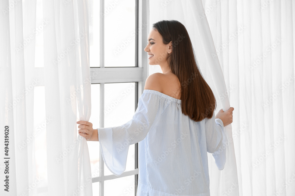 Pretty young woman opening curtains in room Pretty young woman opening curtains in room