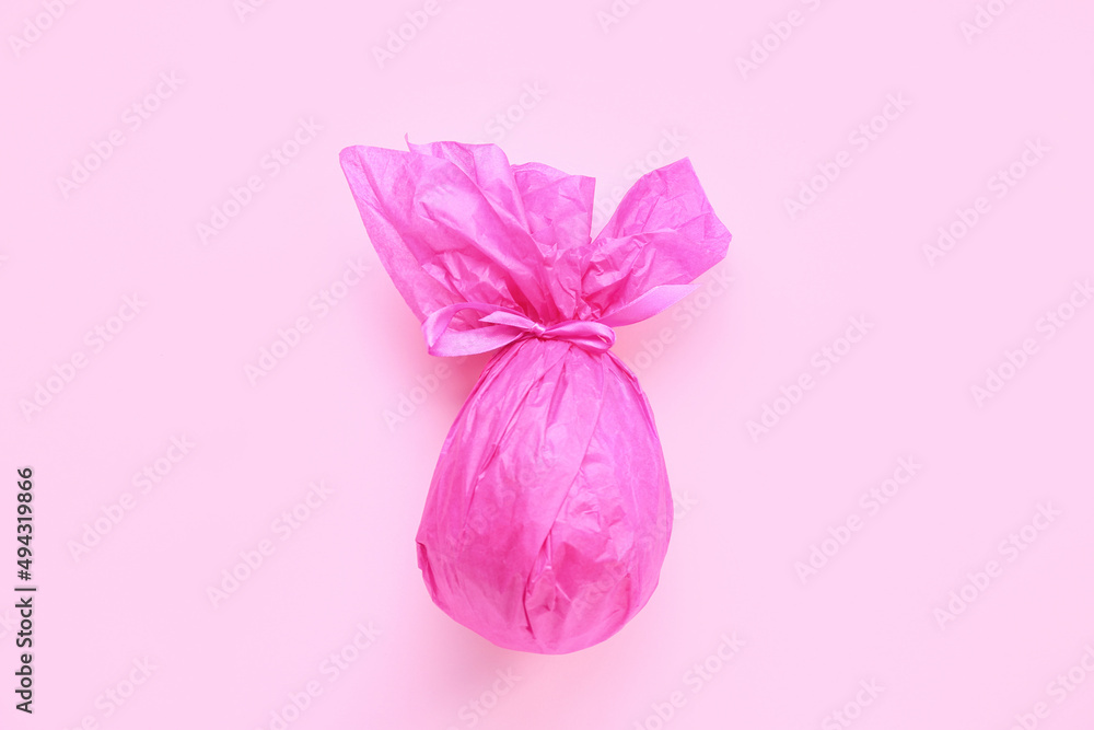 Chocolate Easter egg wrapped in pink paper on color background Chocolate Easter egg wrapped in pink paper on color background