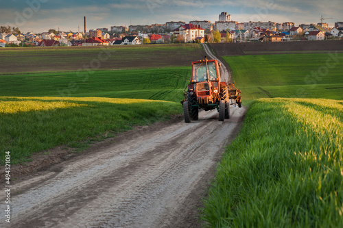 tractor driving on a field road through a green field of winter wheat in the ...