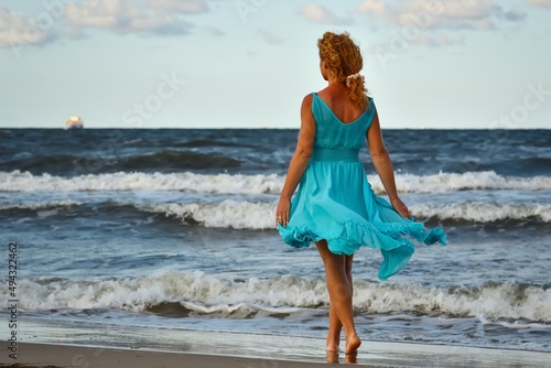 Beautiful blonde haired woman on the beach. Girl in a blue dress at the Polish seaside.