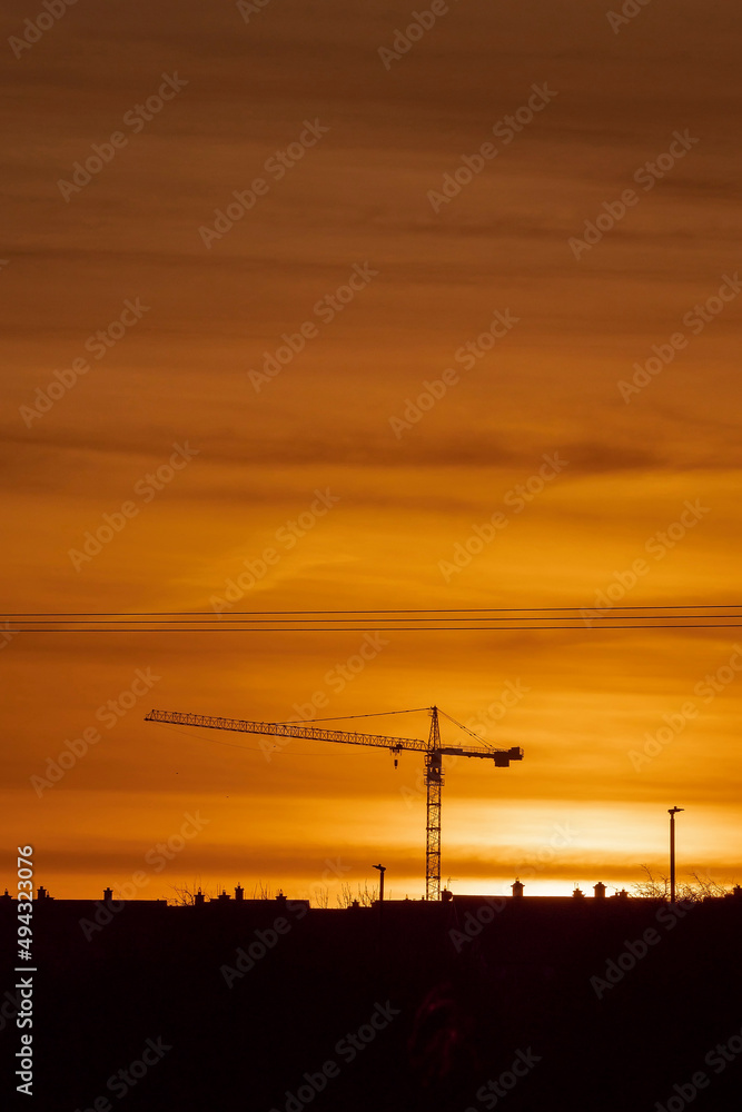 Sunset of sunrise scene. Silhouette of a tall crane against warm orange color sky. Urban construction background. Calm mood.