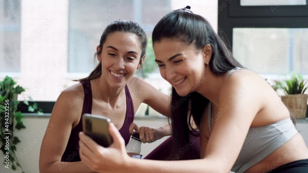 Video of two sporty young women having a break of online gym classes while looking smartphone on floor at home. Video of two sporty young women having a break of online gym classes while looking smartphone on floor at home.