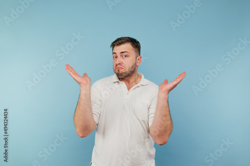 Portrait of a puzzled man with bristles on a blue background, looking at the camera and confusedly spreads his arms photo