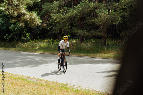 A man in outfit trains on a bicycle in the woods on an asphalt road, quickly rides forward, side view.