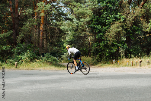 Photo of a sporty man in a bicycle outfit rides in the woods on an asphalt road outside the city on a bicycle and trains.