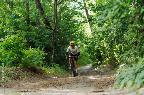 Male cyclist rides off-road in a green summer forest on a bicycle with a serious face, wears professional cycling equipment
