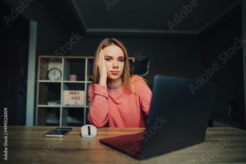 Tired attractive woman sitting at home at the computer and looking at the camera with a sleepy face.