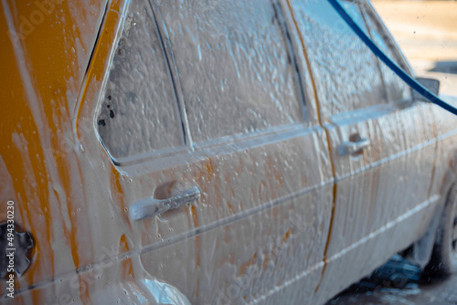 Washing a retro car in yellow color with a high pressure washer.