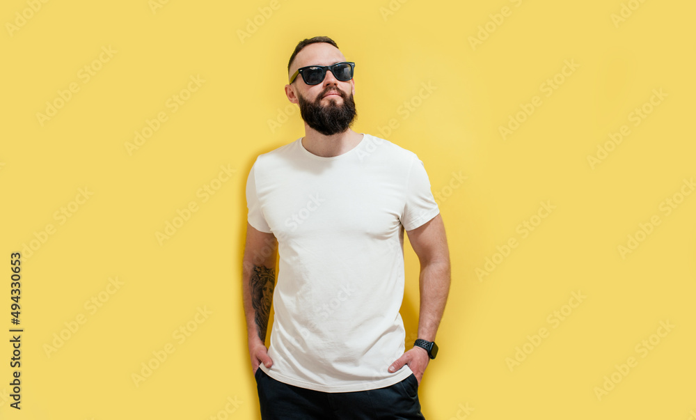 Young bearded hipster guy wearing white blank t-shirt. Studio shot on yellow background. Mock-up for print. T-shirt template.