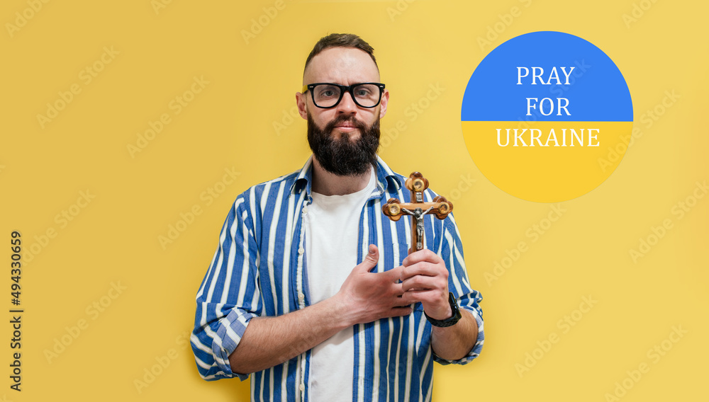 Praying religious man with a cross in his hands prays for Ukraine.