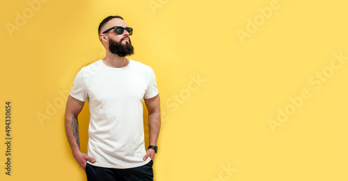 Young bearded hipster guy wearing white blank t-shirt. Studio shot on yellow background. Mock-up for print. T-shirt template. © San4ezz007