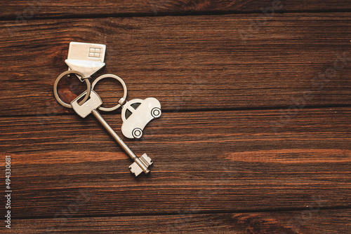 The key to the apartment with a keychain in the shape of a house and car on wooden background.