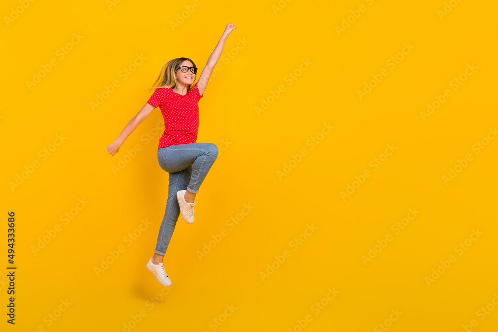 Full body profile side photo of youth active girl jump power hero look empty space isolated over yellow color background Full body profile side photo of youth active girl jump power hero look empty space isolated over yellow color background