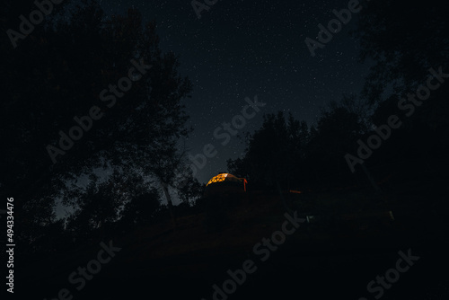 Low angle shot of a lighting itsy bitsy cabin on the hill against night sky full of stars photo