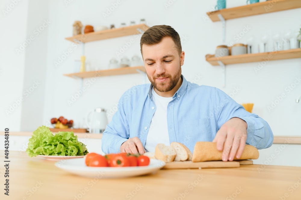 Young man sit at table and cut cucumber on salad Young man sit at table and cut cucumber on salad