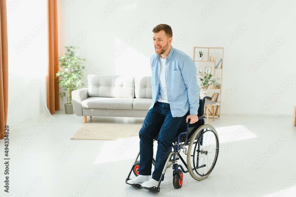 Disabled young guy trying to get up from wheelchair at home, copy space. Disabled young guy trying to get up from wheelchair at home, copy space.