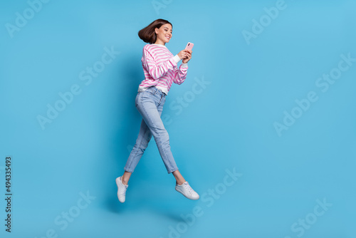 Full length photo of cute young lady run with telephone wear shirt jeans footwear isolated on blue background
