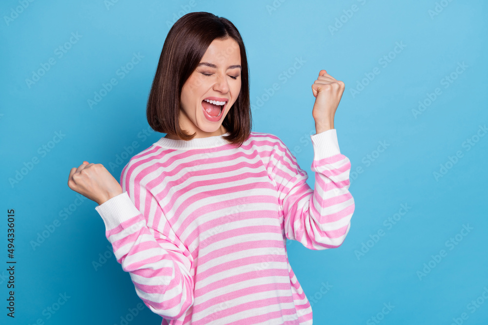 Photo of hooray young lady hands fists yell wear pink shirt isolated on blue color background Photo of hooray young lady hands fists yell wear pink shirt isolated on blue color background