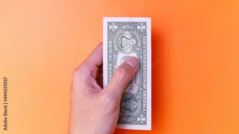 Man's hand is making a payment. Business Investment Economy Saving Loan Income Money and Finance concept. Male hand showing dollar cash on an orange background. One Dollar 1 USD. Prosperity concept. Man's hand is making a payment. Business Investment Economy Saving Loan Income Money and Finance concept. Male hand showing dollar cash on an orange background. One Dollar 1 USD. Prosperity concept.