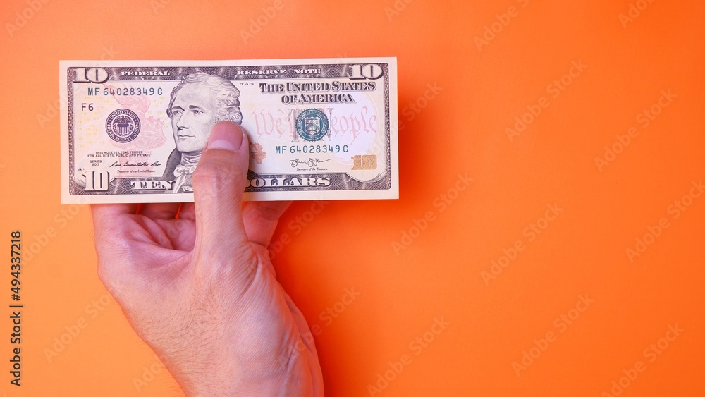 Man's hand is making a payment. Business Investment Economy Saving Loan Income Money and Finance concept. Male hand showing dollar cash on an orange background. Ten Dollar 10 USD. Prosperity concept. Man's hand is making a payment. Business Investment Economy Saving Loan Income Money and Finance concept. Male hand showing dollar cash on an orange background. Ten Dollar 10 USD. Prosperity concept.