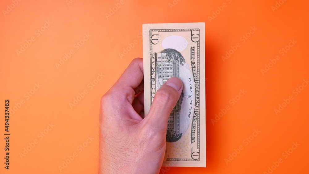 Man's hand is making a payment. Business Investment Economy Saving Loan Income Money and Finance concept. Male hand showing dollar cash on an orange background. Ten Dollar 10 USD. Prosperity concept. Man's hand is making a payment. Business Investment Economy Saving Loan Income Money and Finance concept. Male hand showing dollar cash on an orange background. Ten Dollar 10 USD. Prosperity concept.