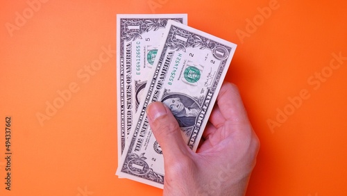 Man's hand is making a payment. Business Investment Economy Saving Loan Income Money and Finance concept. Male hand showing dollar cash on an orange background. One Dollar 1 USD. Prosperity concept.
