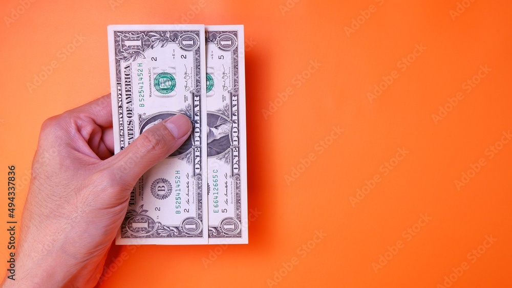 Man's hand is making a payment. Business Investment Economy Saving Loan Income Money and Finance concept. Male hand showing dollar cash on an orange background. One Dollar 1 USD. Prosperity concept. Man's hand is making a payment. Business Investment Economy Saving Loan Income Money and Finance concept. Male hand showing dollar cash on an orange background. One Dollar 1 USD. Prosperity concept.