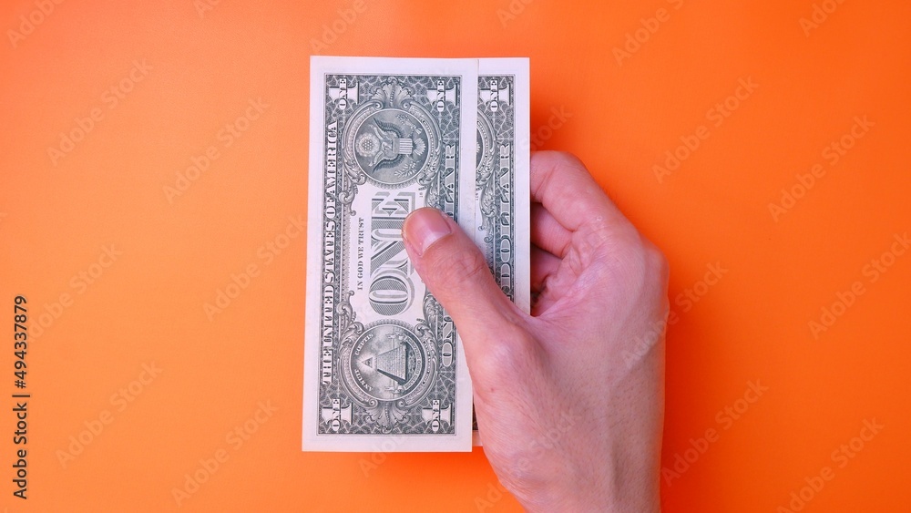 Man's hand is making a payment. Business Investment Economy Saving Loan Income Money and Finance concept. Male hand showing dollar cash on an orange background. One Dollar 1 USD. Prosperity concept. Man's hand is making a payment. Business Investment Economy Saving Loan Income Money and Finance concept. Male hand showing dollar cash on an orange background. One Dollar 1 USD. Prosperity concept.