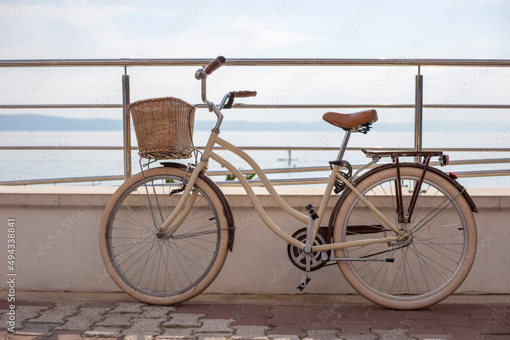 Fototapeta premium White women's bicycle with wicker basket stands on the beach background in summer