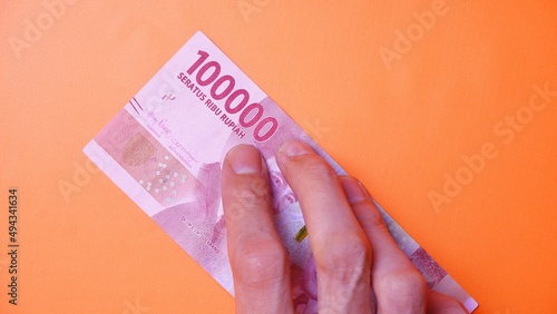 Indonesian Rupiah the official currency of Indonesia. Man's hand is making a payment. Male hand showing Indonesian Rupiah note. Business Investment Economy Loan and Finance concept Uang 100.000 Rupiah