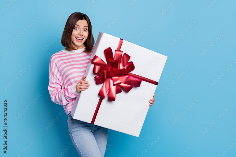 Photo of impressed millennial brunette lady hold large present wear pink jumper isolated on blue background Photo of impressed millennial brunette lady hold large present wear pink jumper isolated on blue background