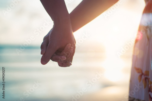 Young adult male groom and female bride holding hands on beach at sunset, copy space for text.