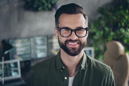 Photo of positive cheerful young man wear green shirt spectacles smiling indoors workshop workplace workstation