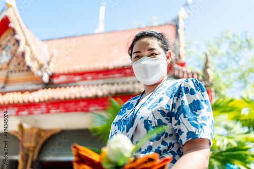 Buddhist woman holding incense sticks, candles, lotus flowers and masks to protect against Covid-19 at Buddhist ceremonies 