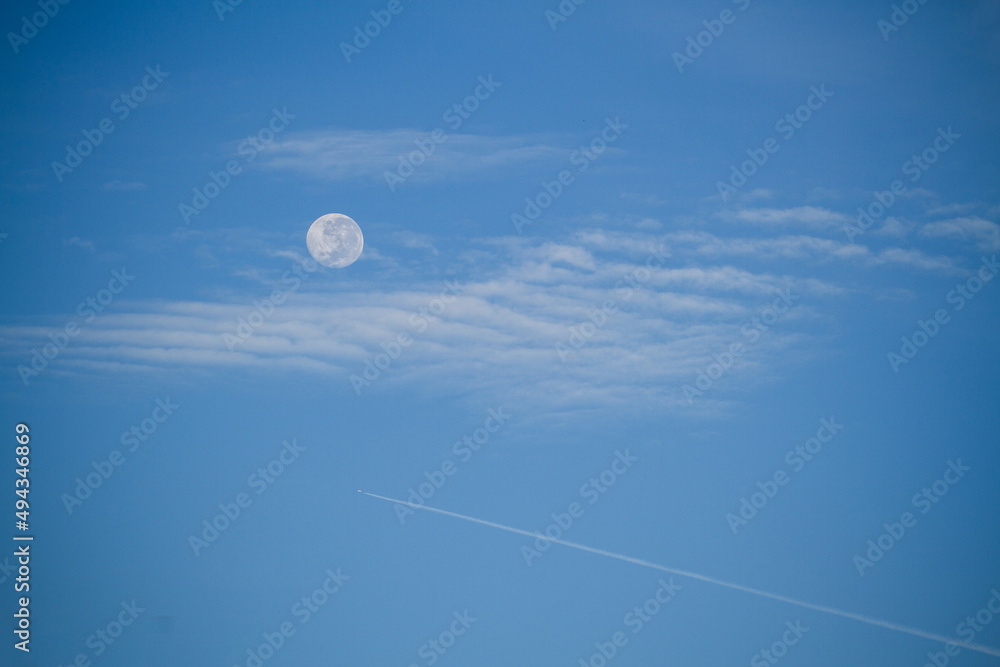 Fototapeta premium Full moon, over the blue sky, clouds and a jet