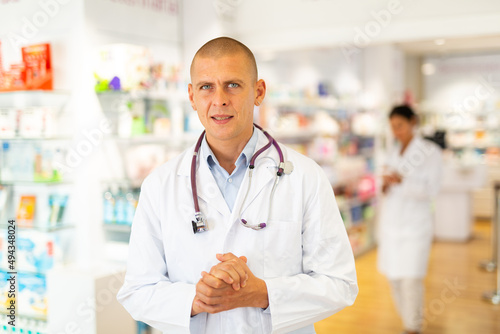 Portrait of male doctor in lab coat standing in salesroom of drugstore.